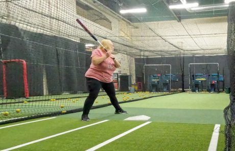 Indoor batting cage with a player practicing hitting on turf, working on swing mechanics during live cage training
