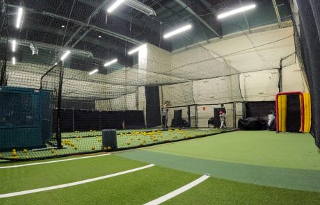 Large indoor batting cage facility with netted lanes, scattered baseballs, and hitters taking swings in professional-grade cages