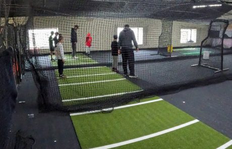 Indoor youth baseball clinic with coaches leading skill drills on turf lanes inside a training facility