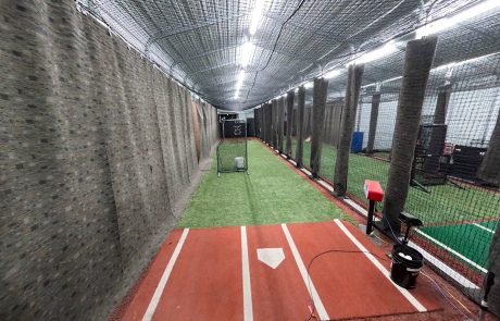 Private baseball lesson batting cage with turf lane, home plate hitting area, pitching screen, and training equipment set up for one-on-one coaching sessions